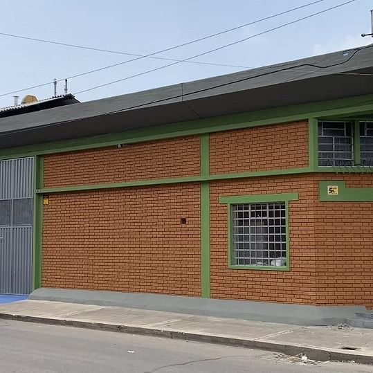 Edificio de ladrillo con detalles verdes, ventanas enrejadas y una puerta metálica gris a lo largo de una calle.