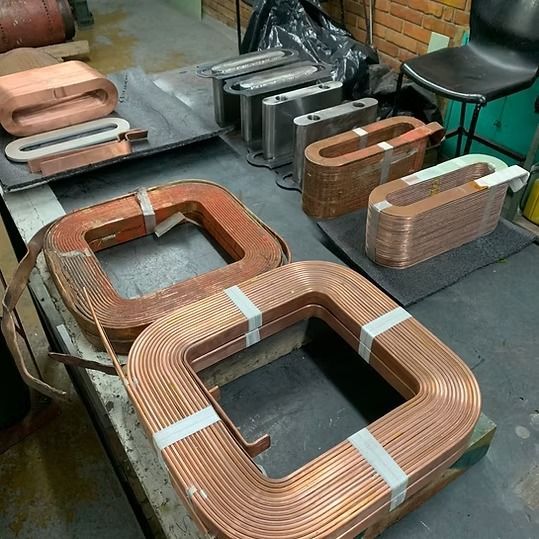 Diversos componentes de bobina cuadrada de color cobre dispuestos en el suelo y la mesa de un taller.