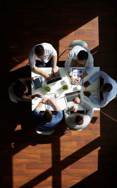 a group of people are sitting around a table with laptops .
