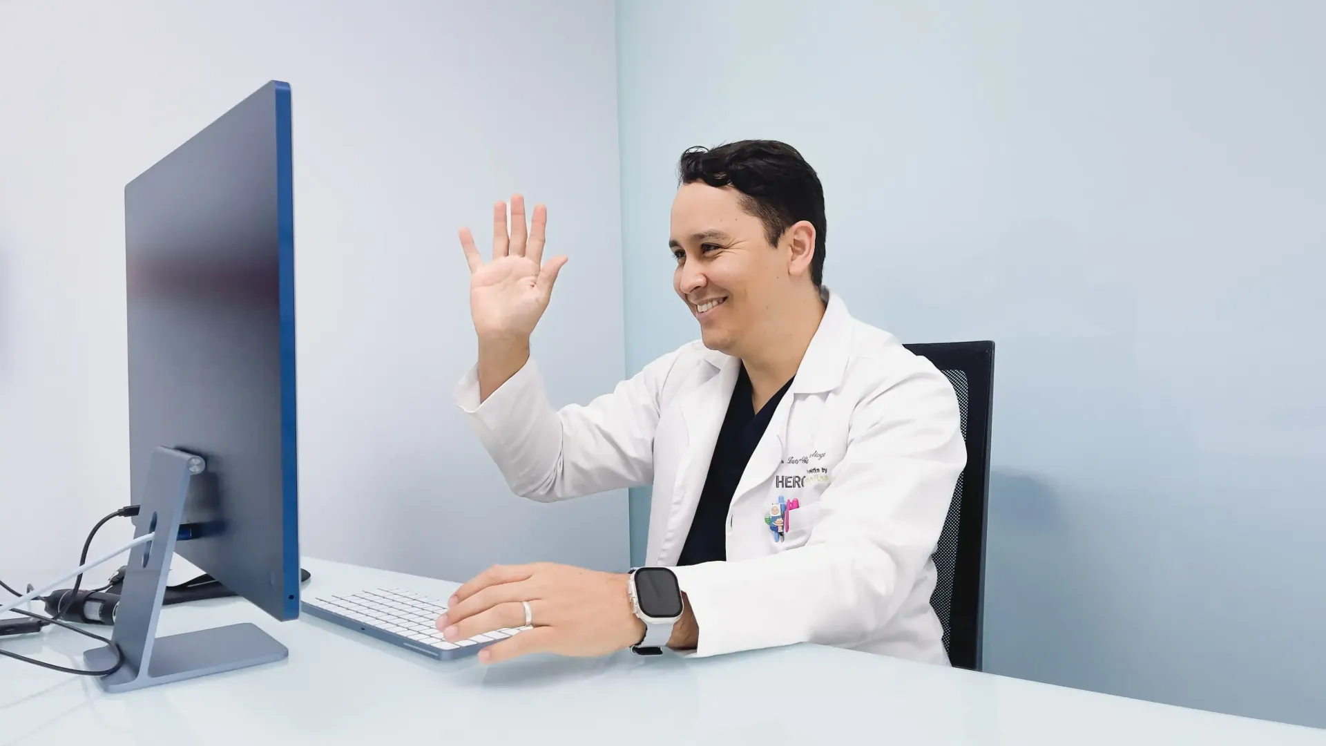 a male doctor is sitting at a desk using a laptop computer .