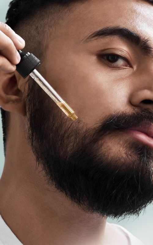 a man with a beard is applying a dropper to his beard .