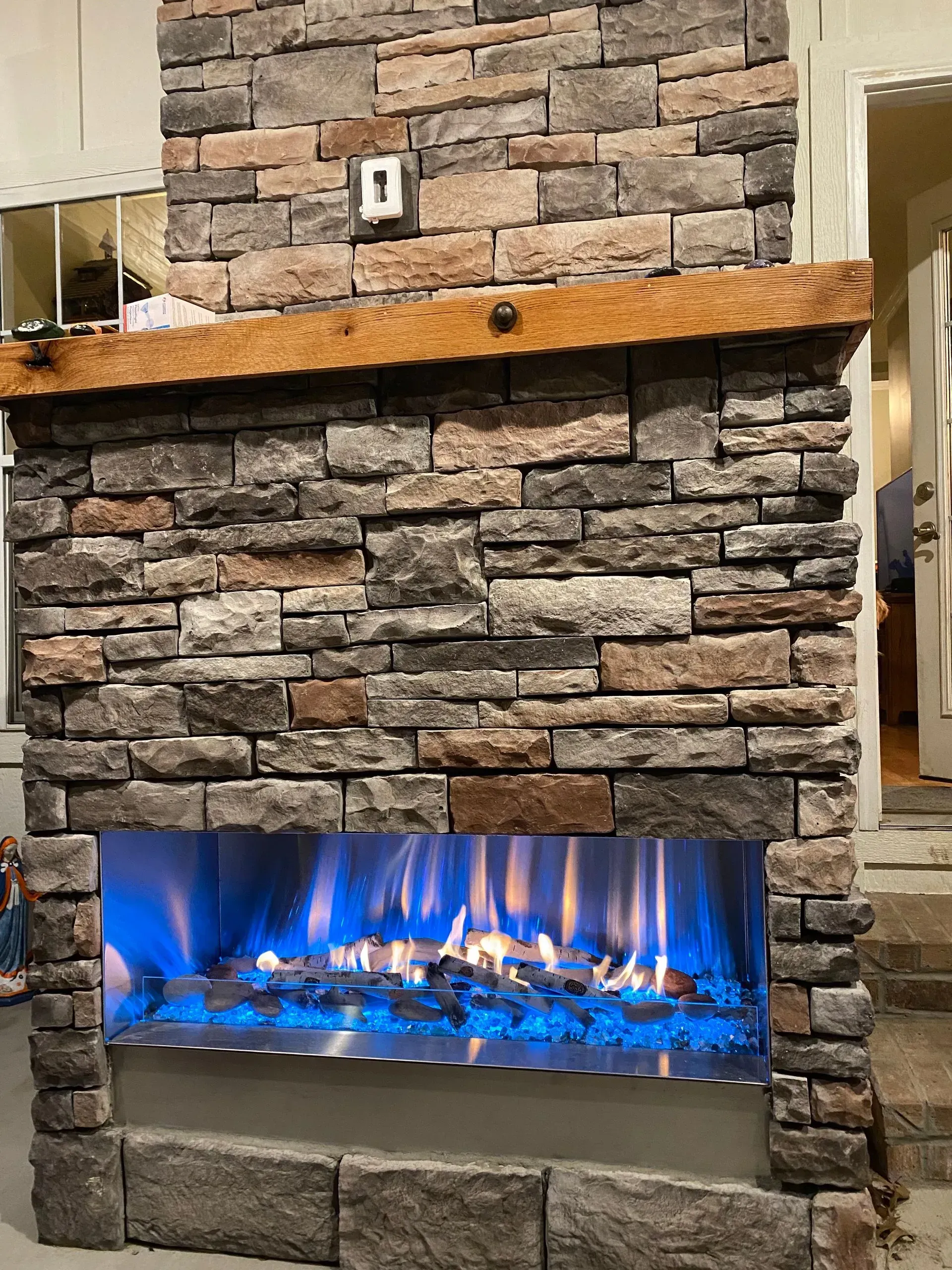 Stone fireplace with blue flames, glass rocks, and a wooden beam mantel.