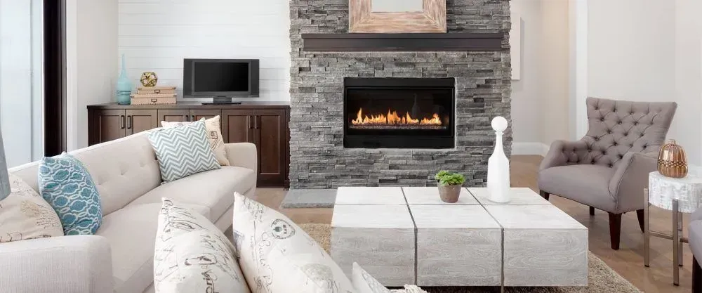 Living room with stone fireplace, TV, cream couch, and gray armchair.
