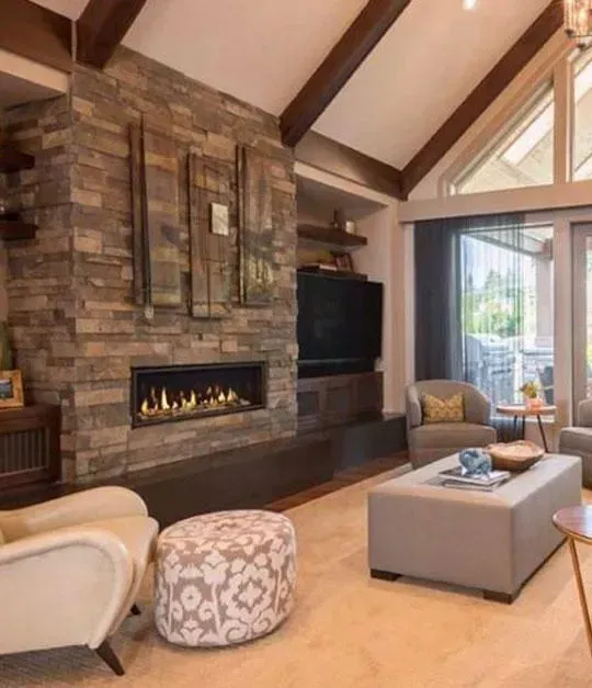 Living room with stone fireplace, TV, and seating. Beige and brown tones; vaulted ceiling.