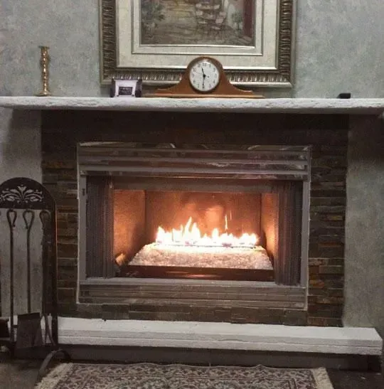 Fireplace with lit flames, stone surround, mantel clock, artwork, and decorative accessories.
