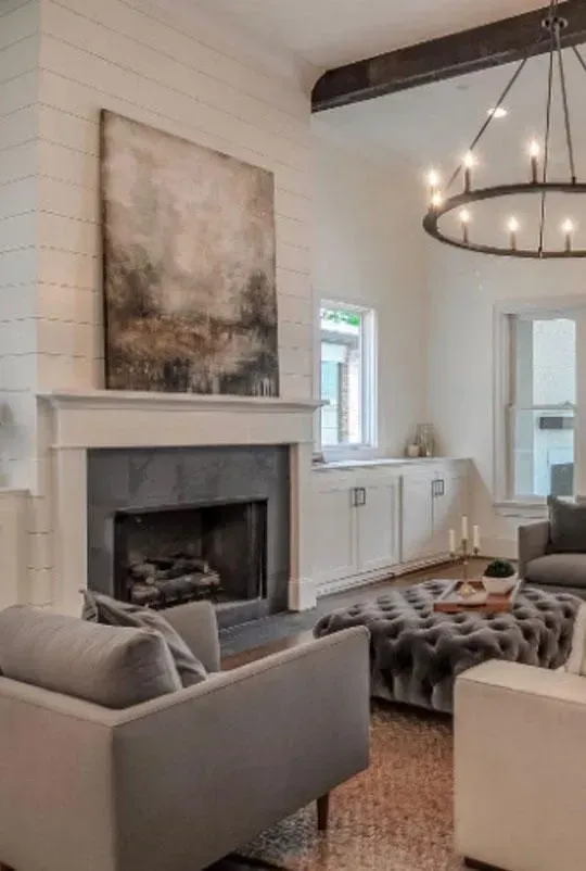 Living room with fireplace, gray furniture, large painting, and a round chandelier.