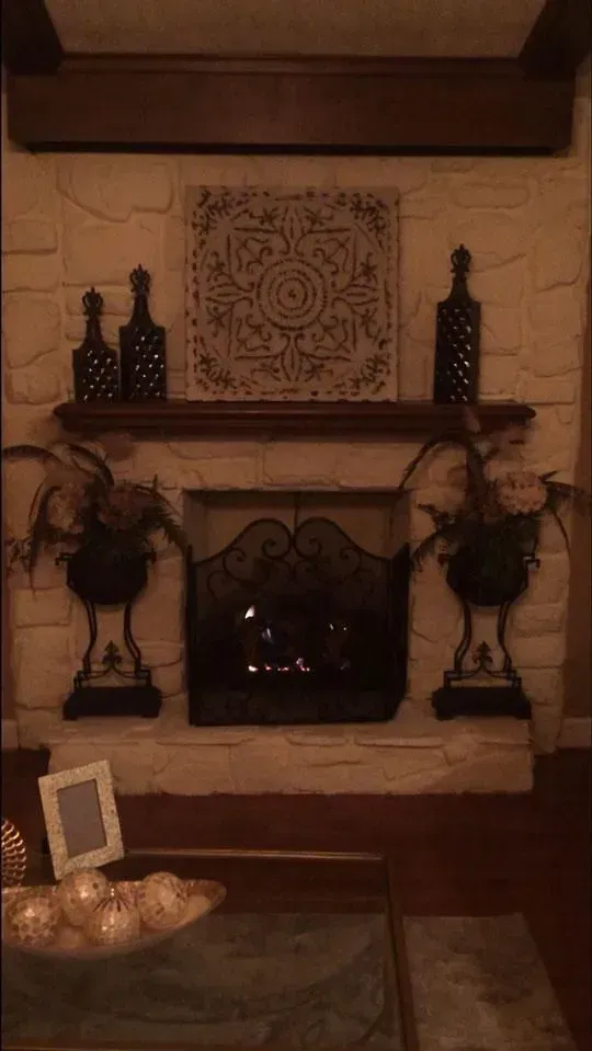 Fireplace with ornate metal screen, decorations, and a lit fire in a cozy living room.
