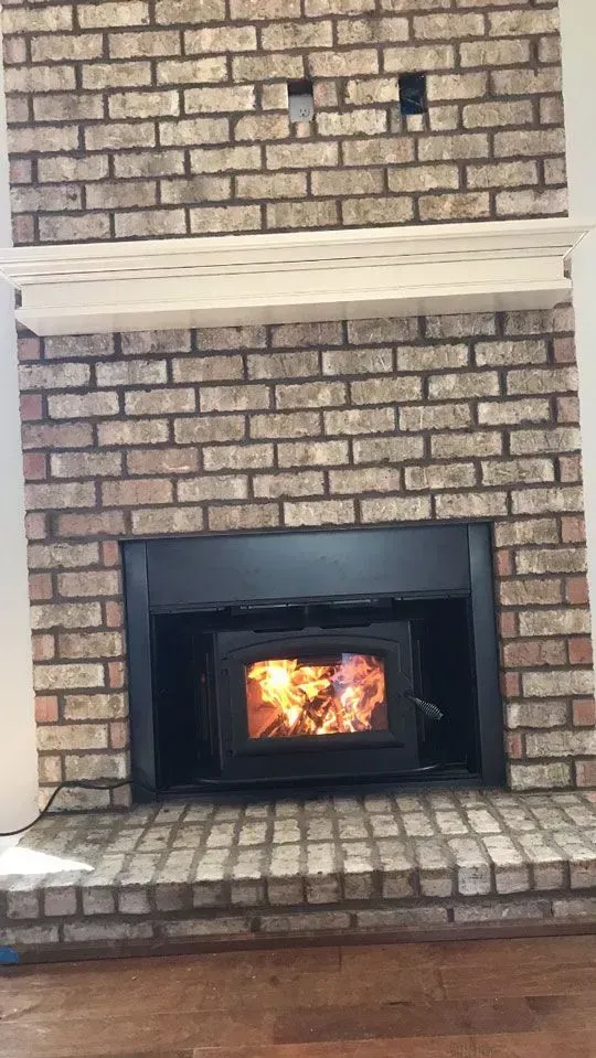 Fireplace with burning fire, set into brick wall. Wooden mantle above.