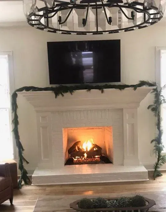 Fireplace with lit fire, TV above, and garland. Light-colored walls and wood floors.