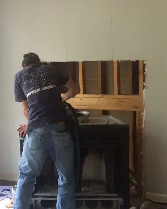 Man working on a fireplace. The wall is open, revealing the wooden frame.