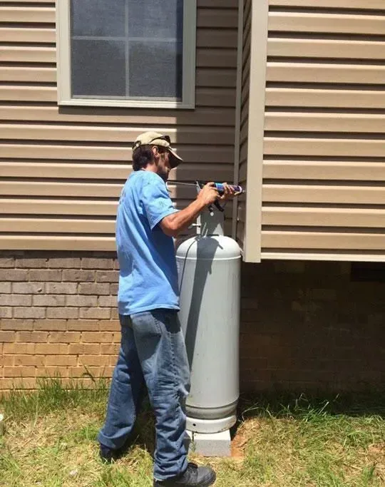 Person filling propane tank next to a house with tan siding, next to a window.