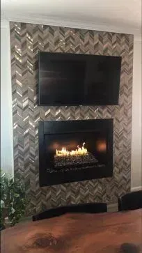 Fireplace with lit flames and a mounted TV on a tiled accent wall.