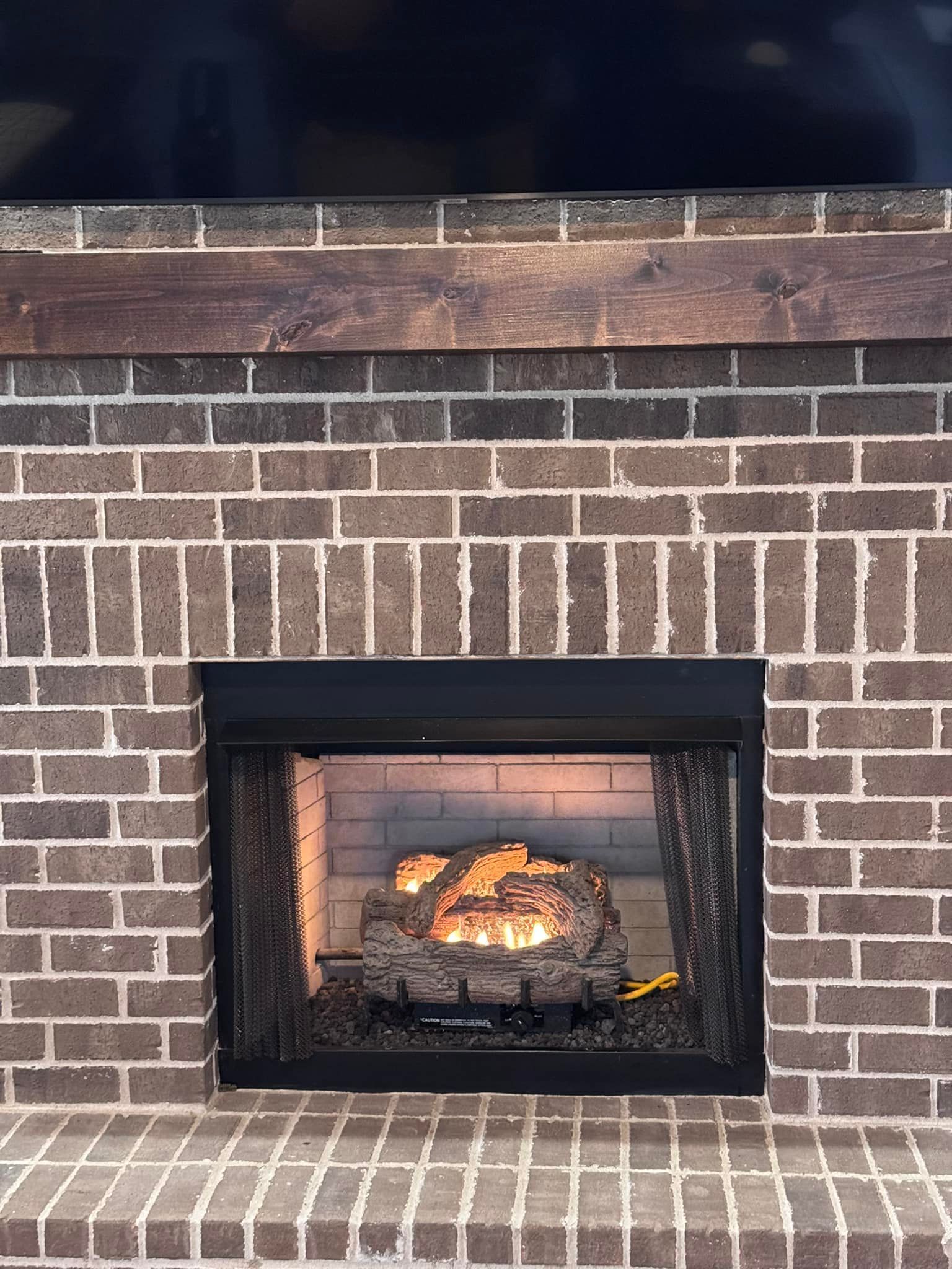 Brick fireplace with dark mantel and burning gas logs.