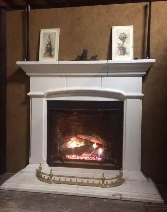 A white fireplace with a burning fire, two framed pictures above, and a brass screen.