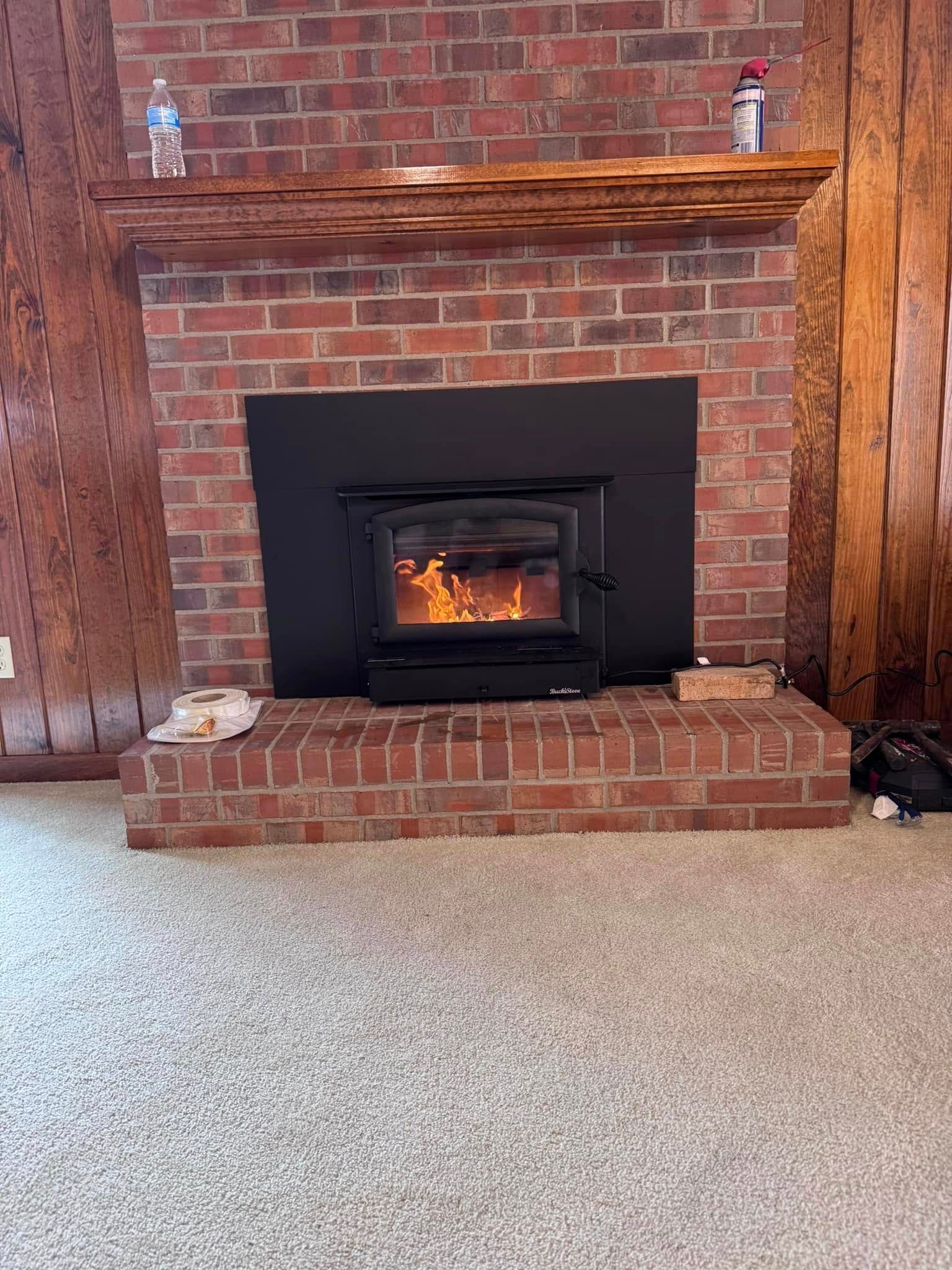A brick fireplace with a burning wood stove; a wooden beam and items are on the mantle.