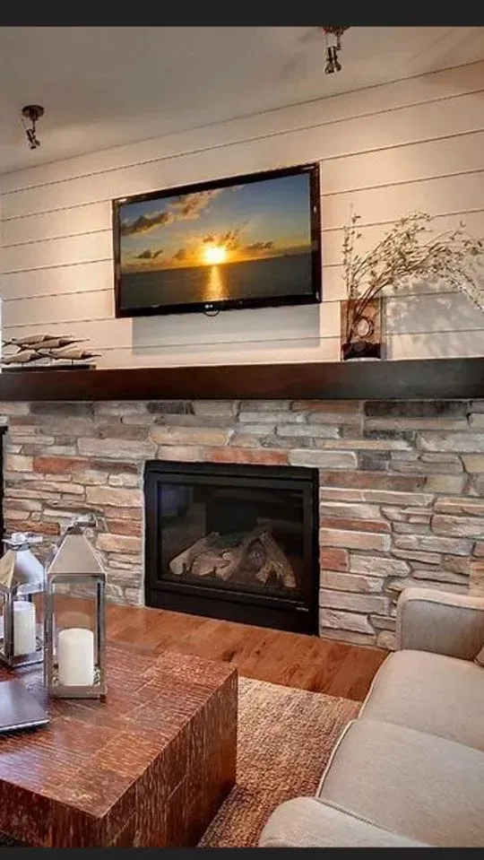 Living room fireplace with stone and wood details. TV above fireplace.