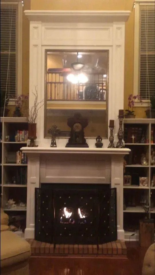Fireplace with black screen, white mantel, and mirror reflecting a second floor.