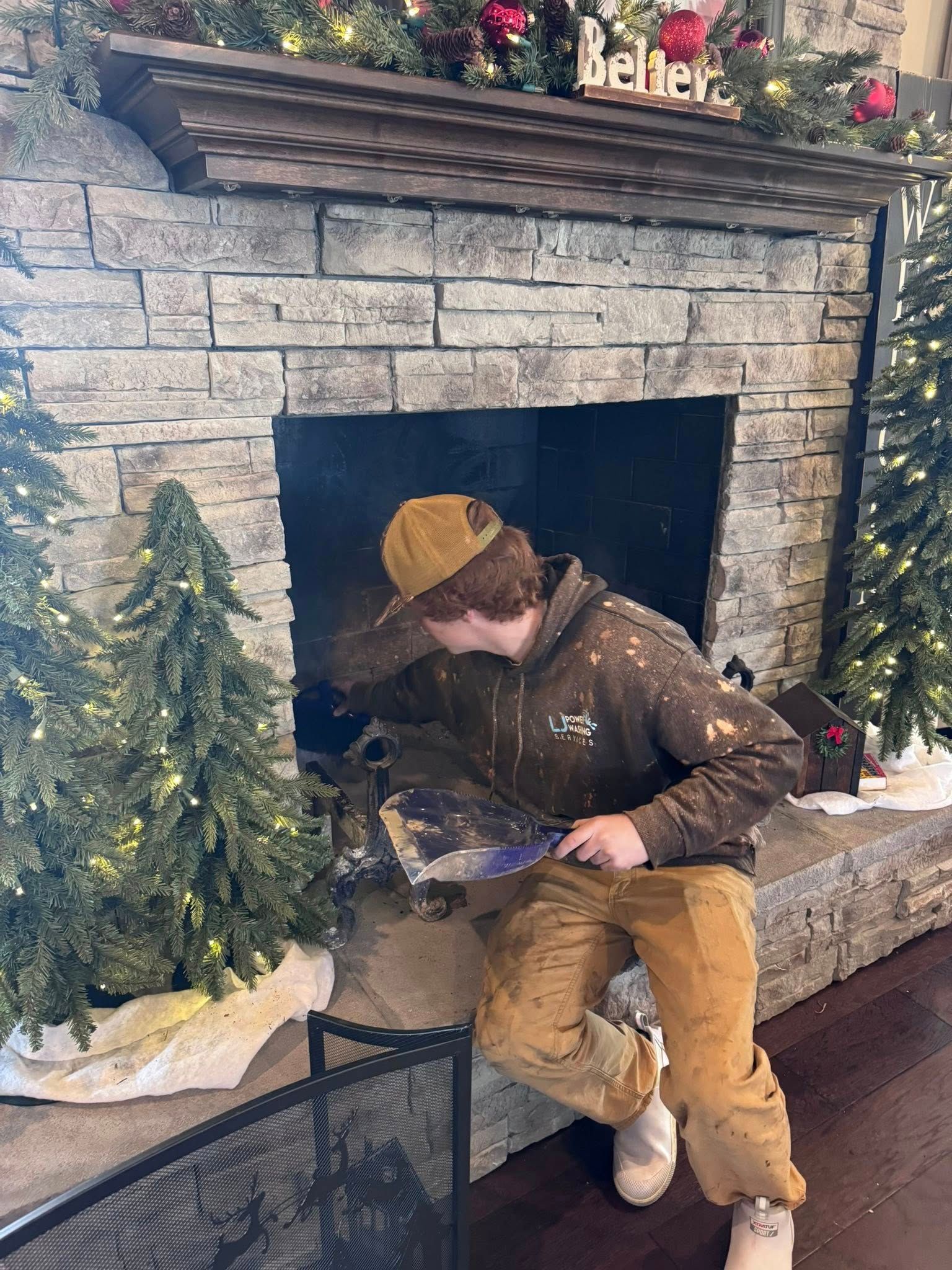Person cleaning fireplace, wearing brown work clothes and hat, with decorations.