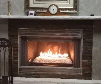 Fireplace with flames and decorative mantel. Brown stone surround. Clock, frame, and small statues on the mantel.