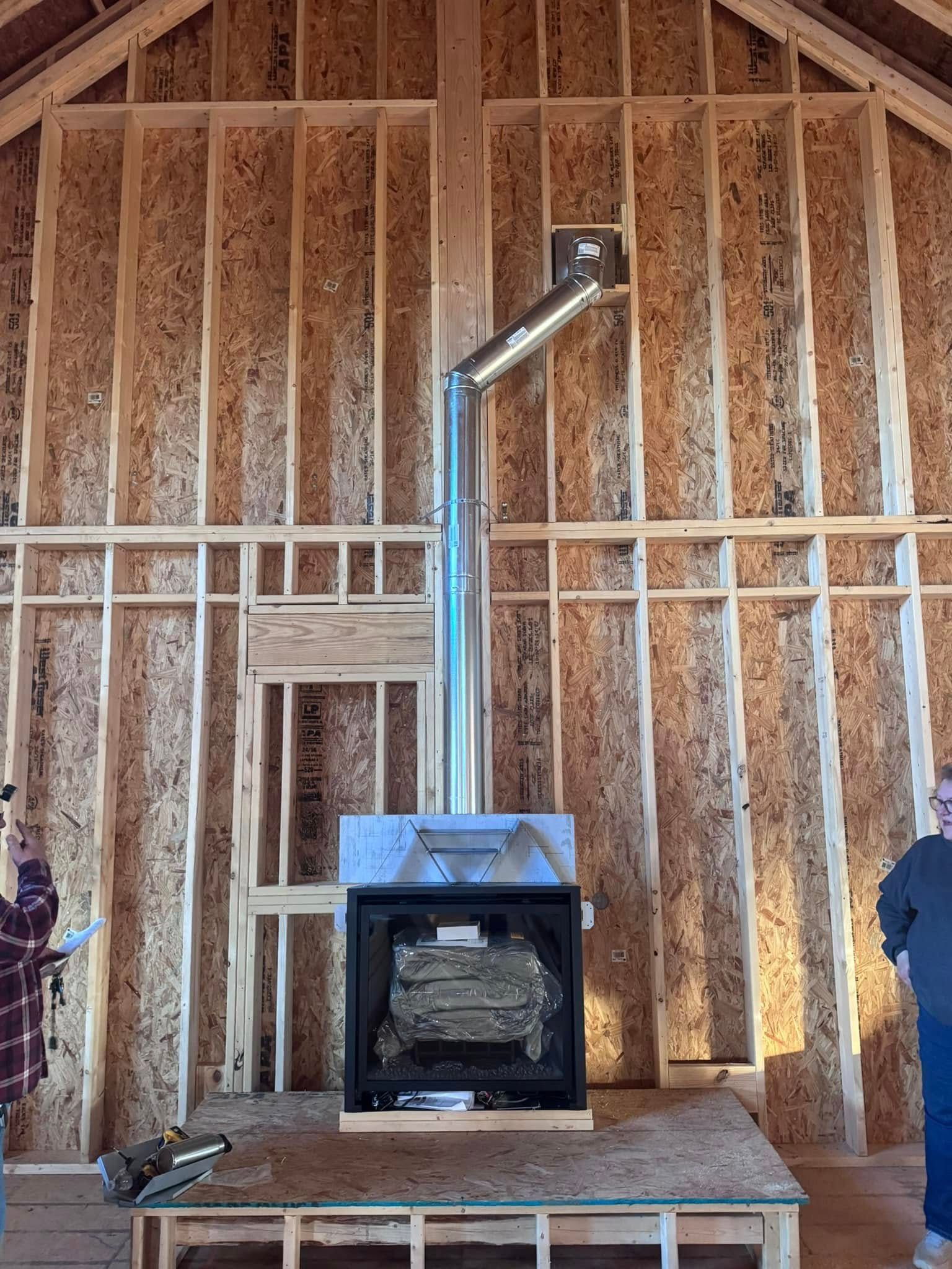 Wood stove installed in a wooden framed building. Silver chimney pipe extends upward.