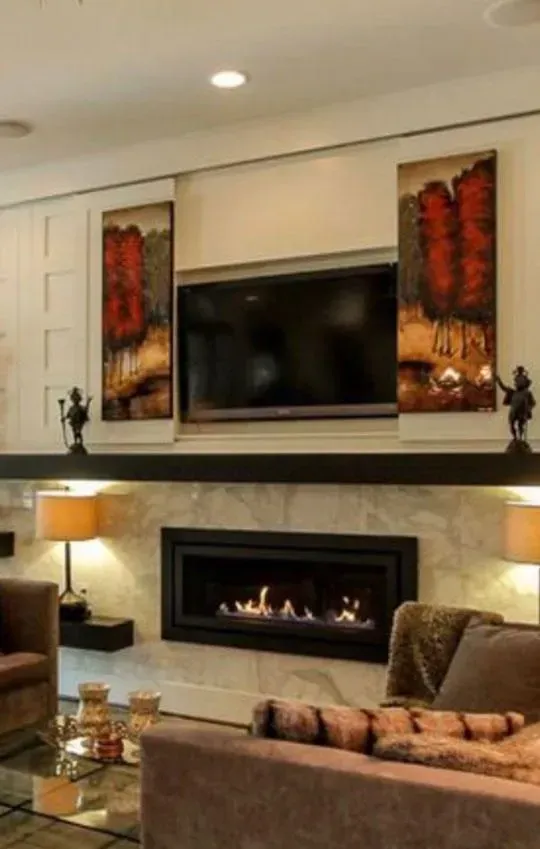 Living room fireplace with a TV, art, and furniture. Warm lighting and brown color scheme.