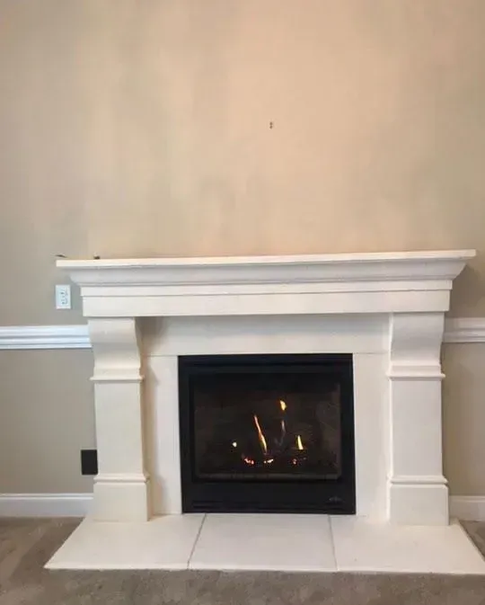 White fireplace with burning flames, beige walls, and white trim.