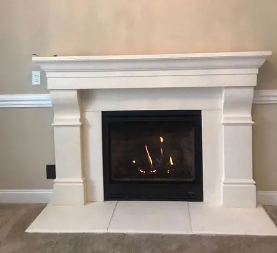 White fireplace with a lit fire, set against a neutral wall.