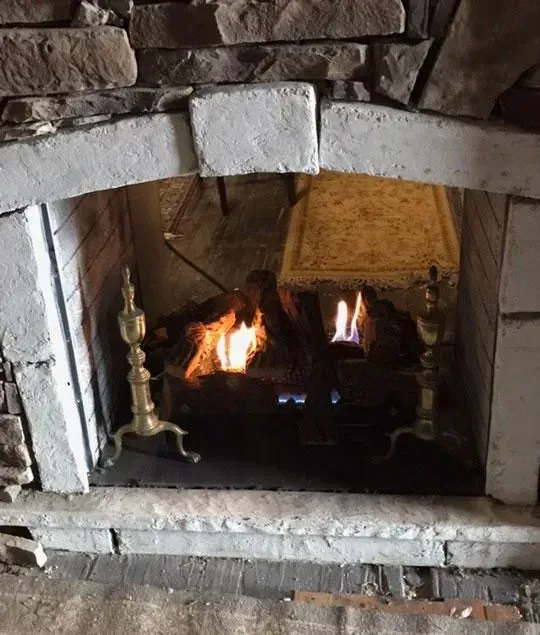 Fireplace with burning fire, brass candlesticks, and a decorative table inside.