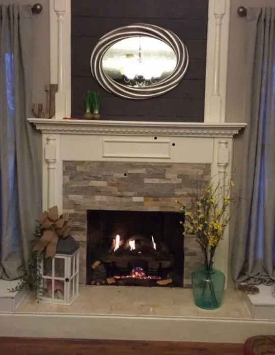 Fireplace with stacked stone facade, framed by white molding, topped with a mirror and dark wooden panel.