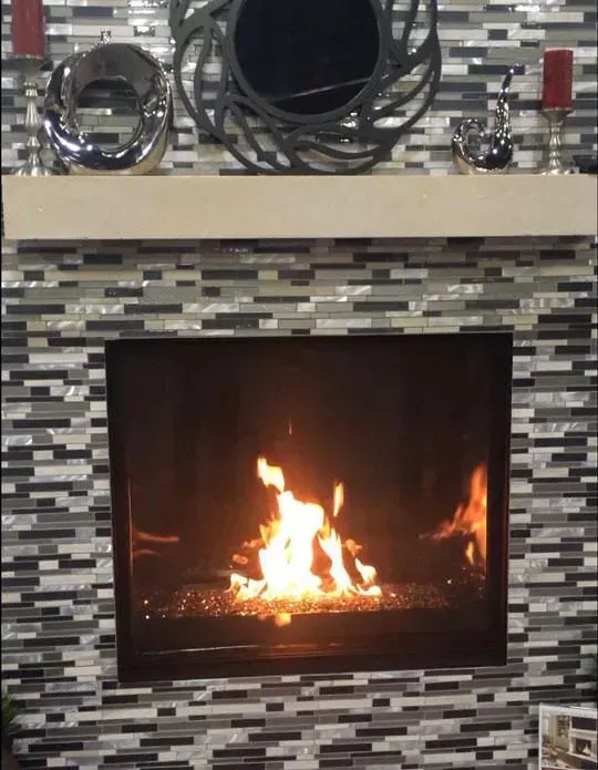 Fireplace with lit fire surrounded by mosaic tile, topped with decorations and a mirror.