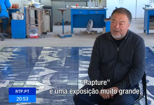 Um homem está sentado no chão em frente a uma placa do rtp.pt
