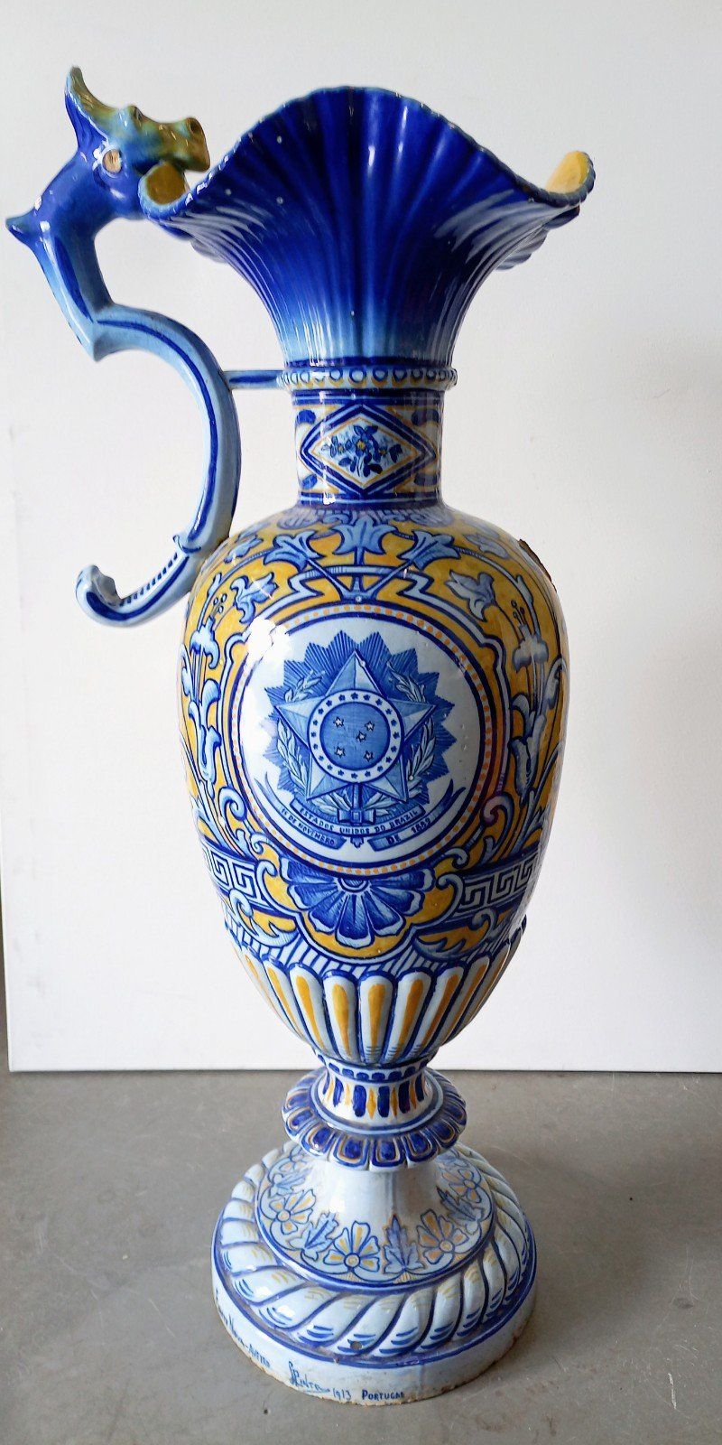 Um vaso azul e amarelo com uma alça está sobre uma mesa.