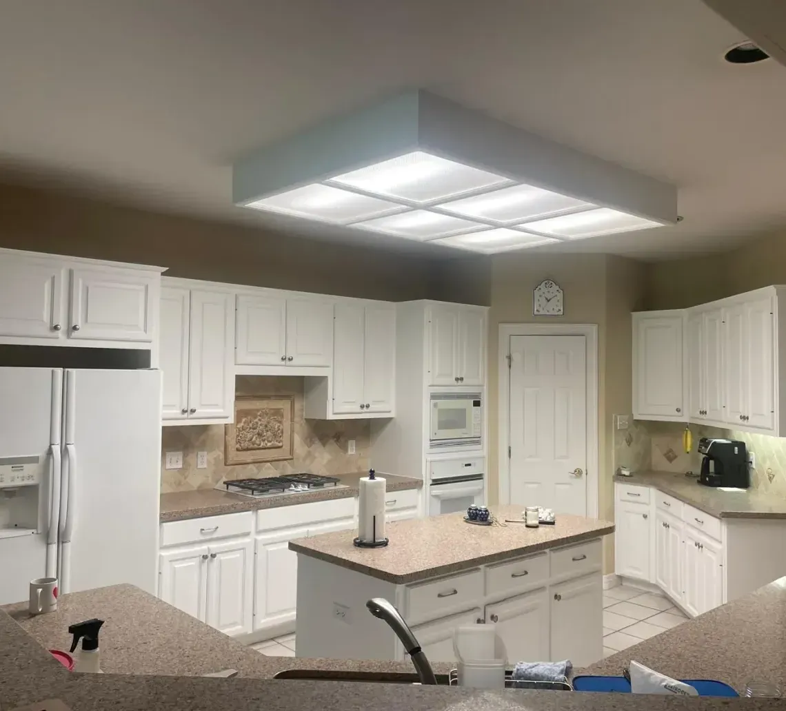 A spacious kitchen with white cabinets, beige countertops, a central island, and a large recessed light fixture.