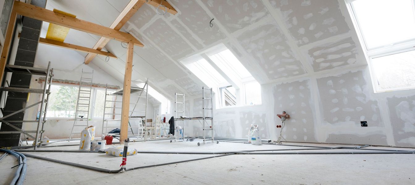 Bright unfinished attic room under renovation with drywall, scaffolding, and large skylights
