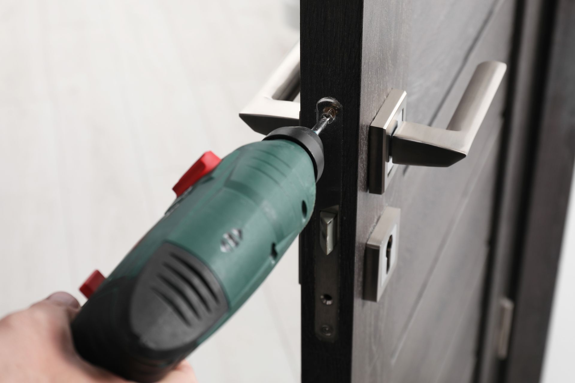 A hand drills a door latch with a green power tool during installation.