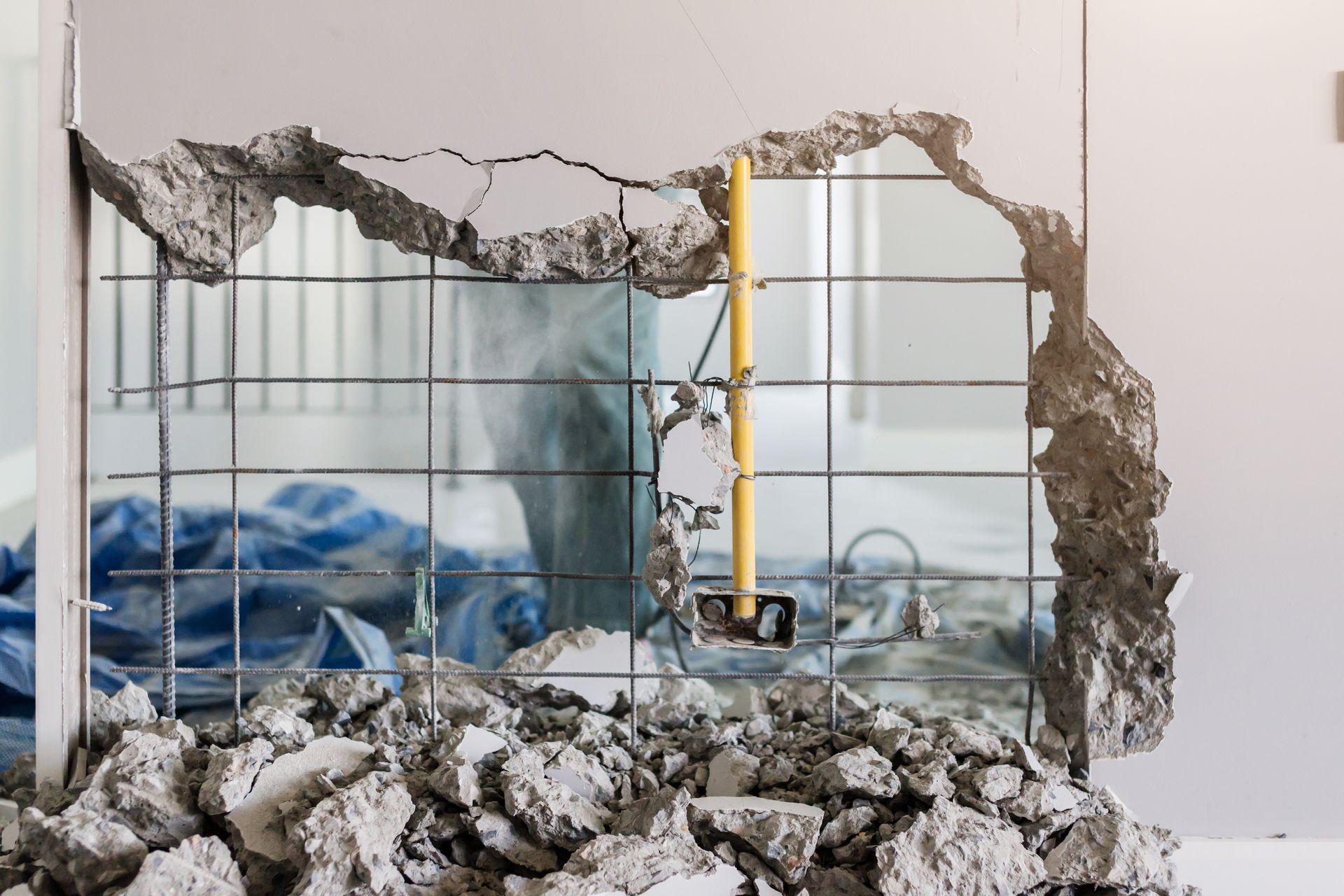 Partially demolished wall revealing construction debris and a room with blue tarps and exposed piping