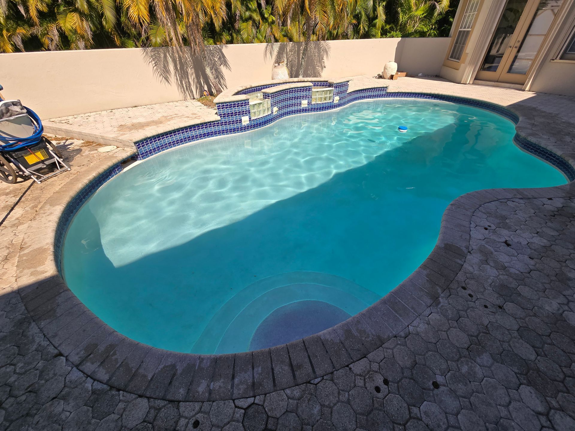 Pool with turquoise water, mosaic tile accents, and a stone deck in a sunny outdoor setting.