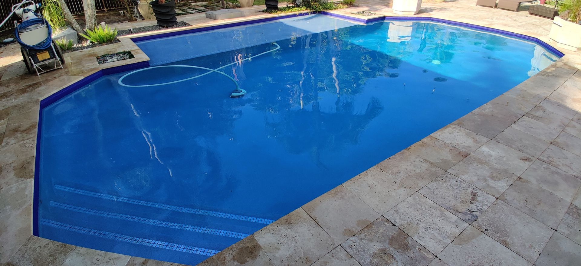 A blue swimming pool with stone stairs and a stone patio.