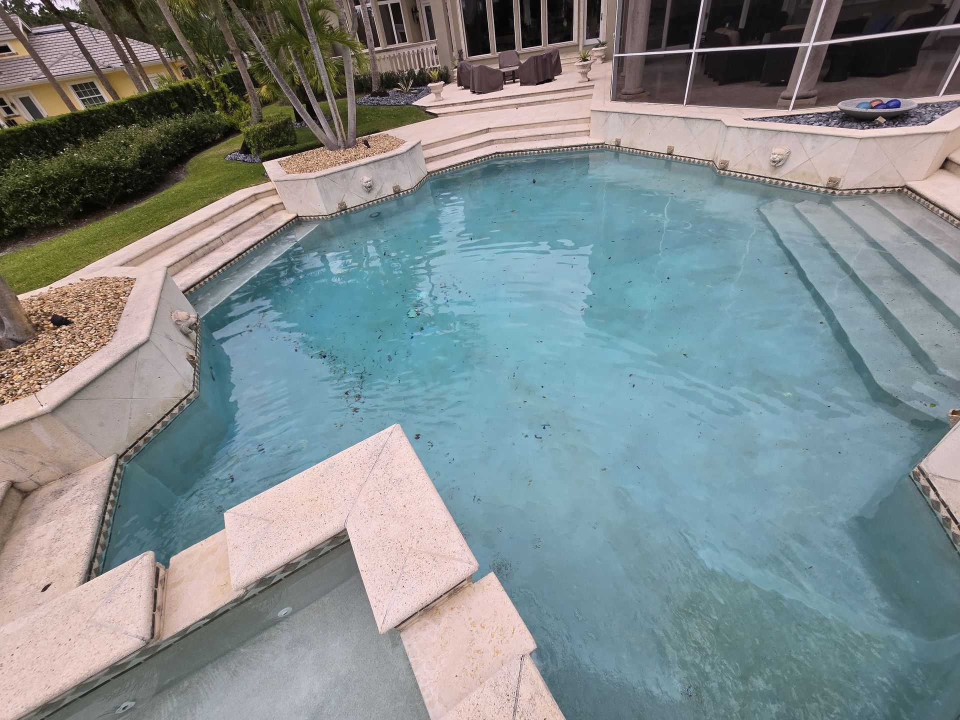 A pool with light blue water, surrounded by steps and a patio, with a building in the background.