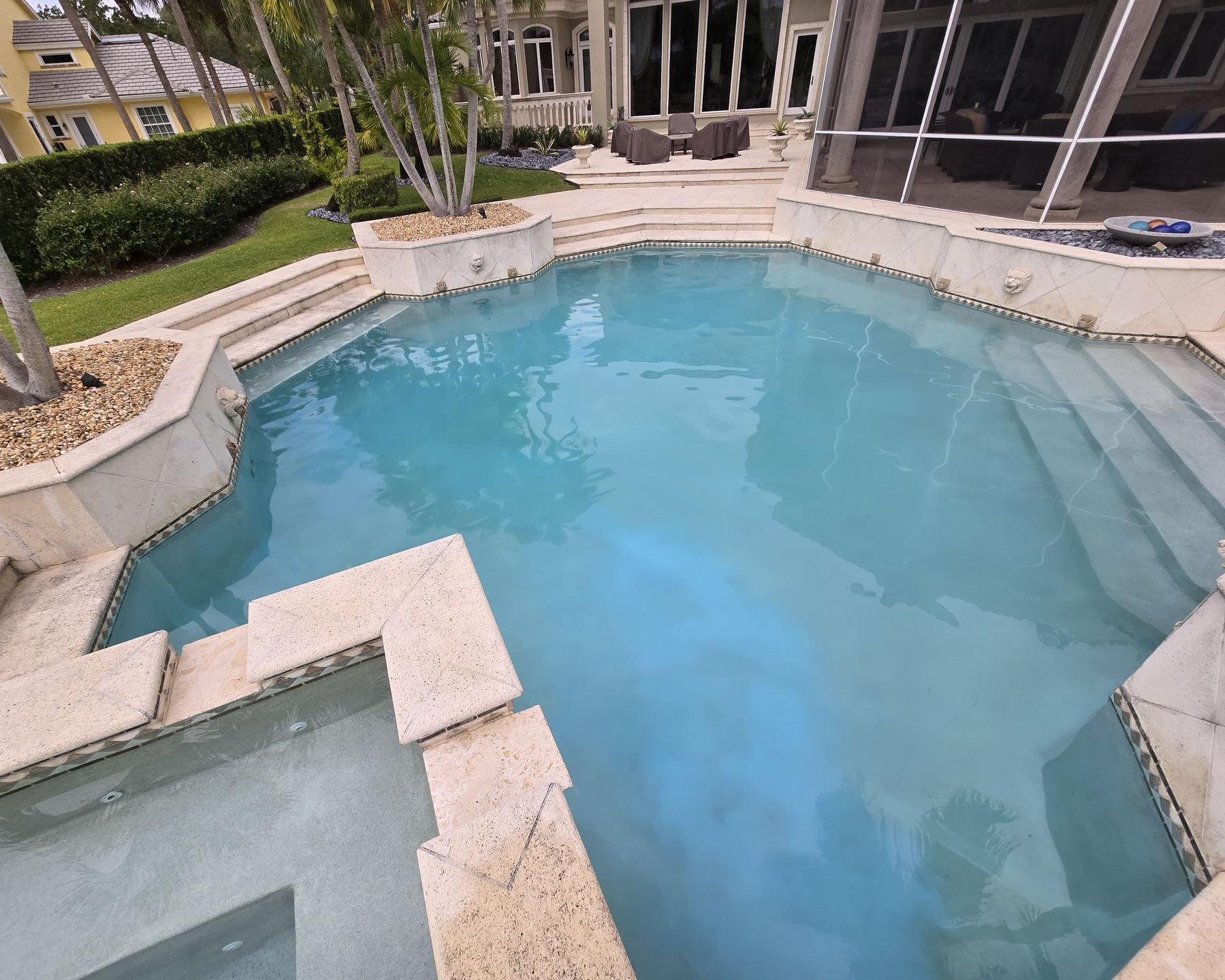 Swimming pool with blue water surrounded by stone steps. House in the background.
