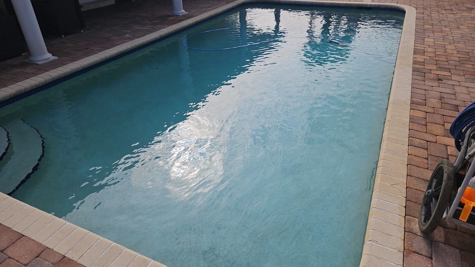 Rectangular swimming pool with blue-green water and brickwork surround, reflecting sunlight.