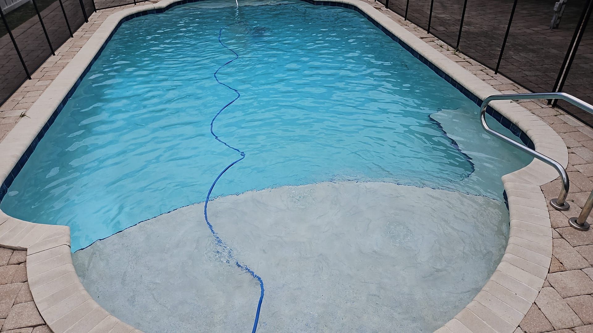 Swimming pool with clear blue water, light concrete surround, steps, and a pool cleaner hose.