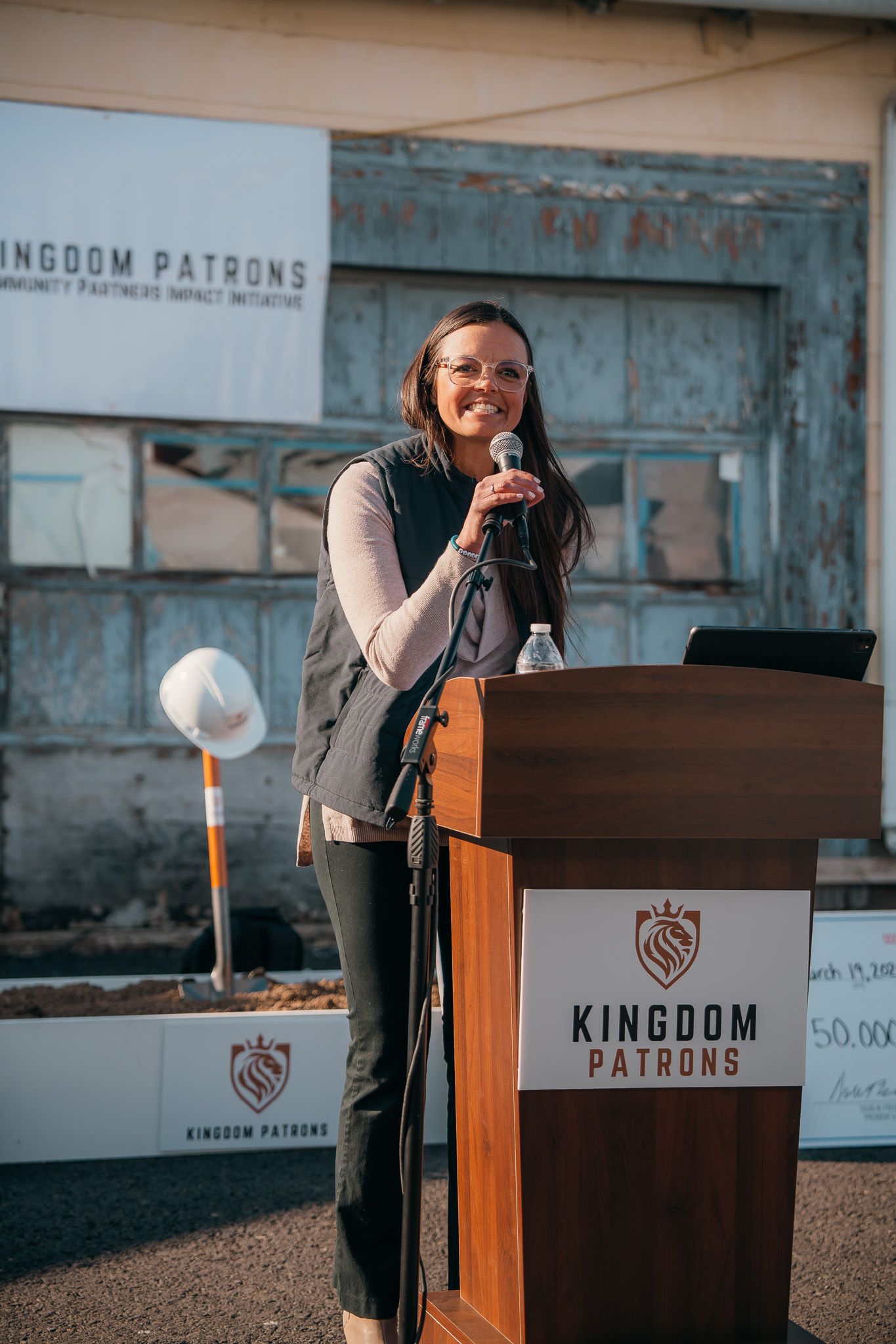 Woman speaking at a podium with a KINGDOM PATRIOTS sign behind her outdoors