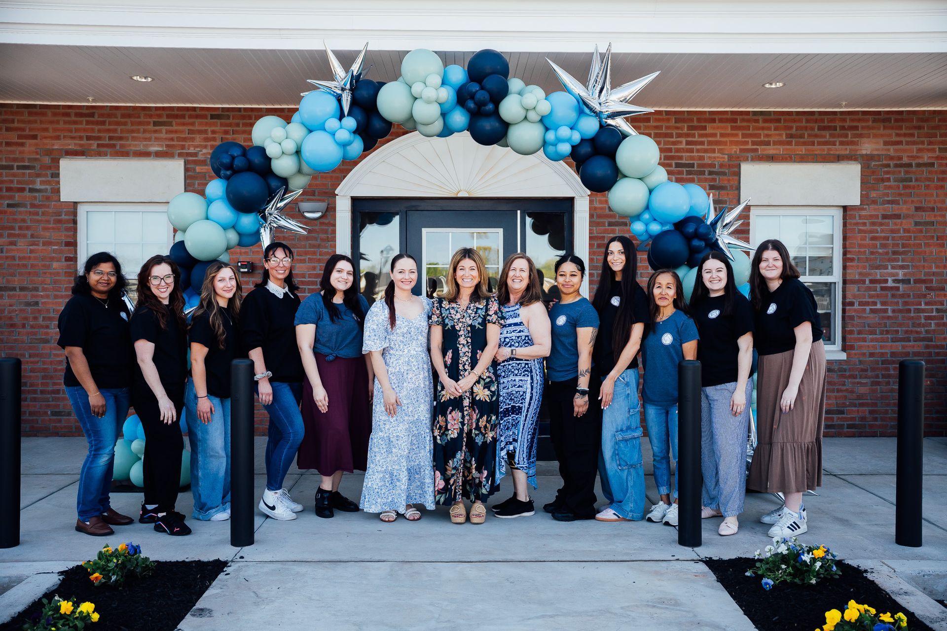 Group posing under blue and white balloon arch at a brick building entrance
