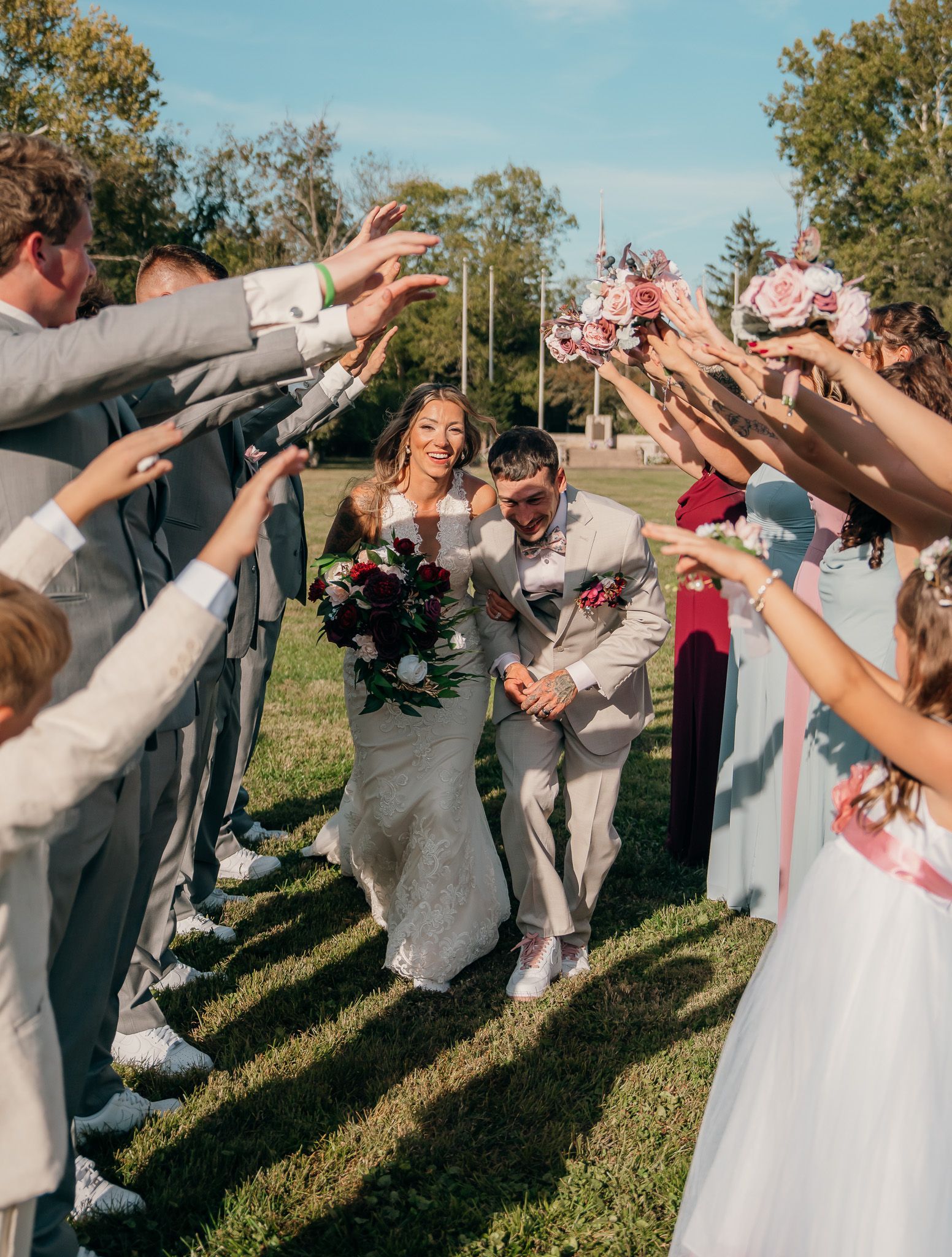 Wedding couple walking under raised arms and flower petals on a sunny outdoor lawn