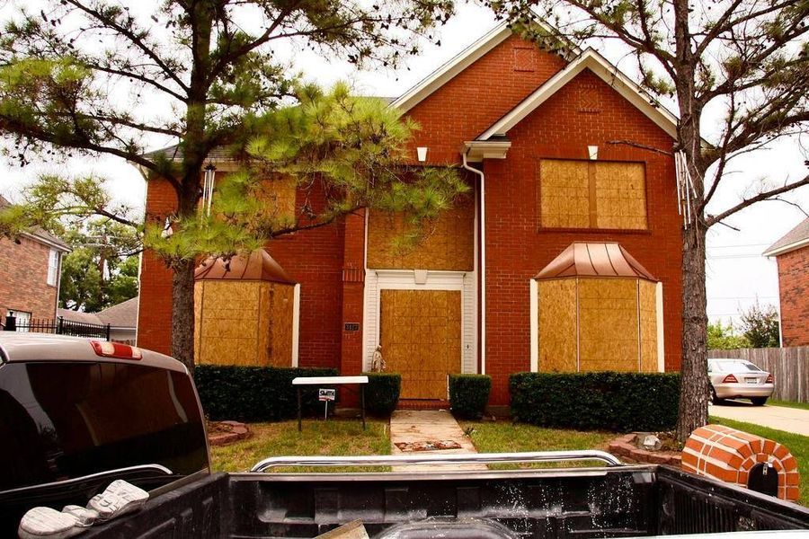 Red brick house boarded up for hurricane, with a pickup truck in front.