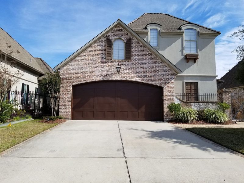 Two-story house with brick and stucco facade, brown garage door, arched window, and driveway.