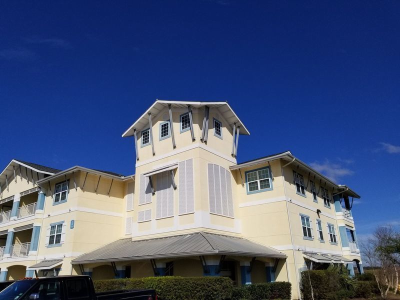 Yellow and white building with blue shutters and trim against a bright blue sky.