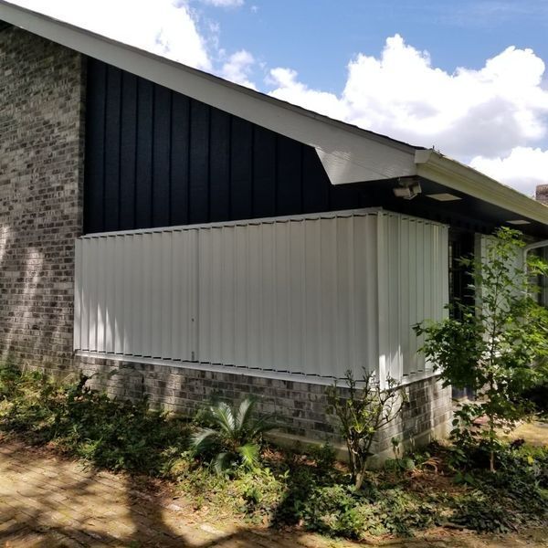 Exterior of a house with white siding, brick, and dark blue paneling. Overcast sky with green plants.