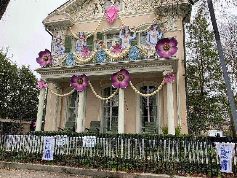 A decorated house with floral cutouts, banners, and figures on the balcony; pink and purple colors.